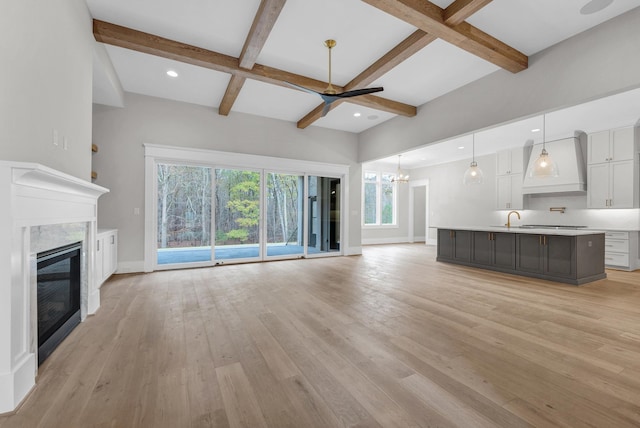 unfurnished living room with light hardwood / wood-style flooring, ceiling fan with notable chandelier, beamed ceiling, and sink