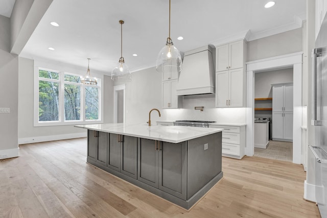 kitchen featuring light hardwood / wood-style flooring, an island with sink, custom range hood, and decorative light fixtures