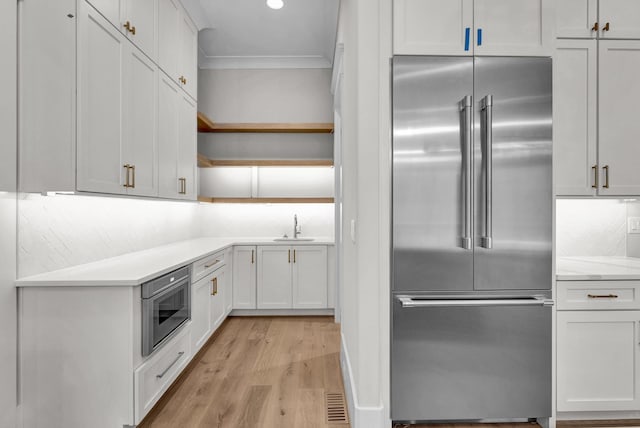 kitchen with built in appliances, sink, backsplash, white cabinetry, and light wood-type flooring