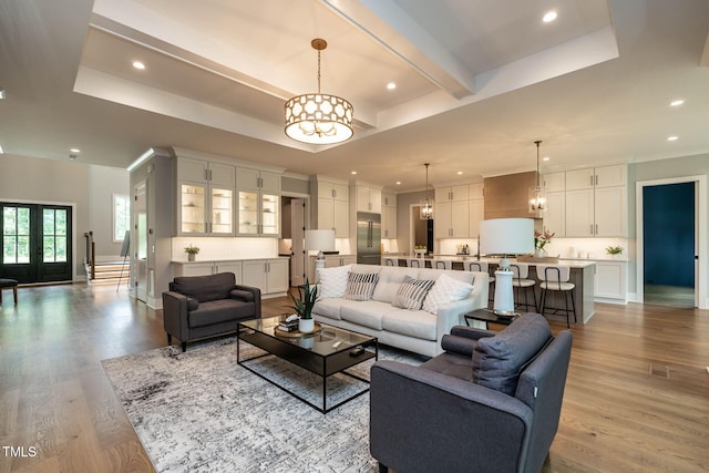 living room featuring light hardwood / wood-style flooring, french doors, a chandelier, and a raised ceiling