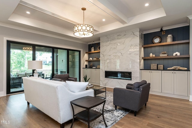 living room with hardwood / wood-style flooring, a premium fireplace, a tray ceiling, and built in features