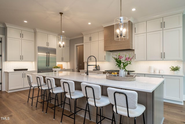 kitchen with appliances with stainless steel finishes, a kitchen island with sink, hardwood / wood-style flooring, and hanging light fixtures