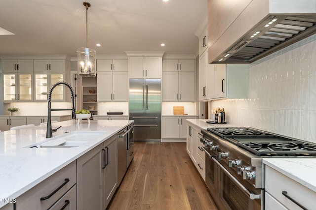 kitchen featuring premium range hood, hardwood / wood-style flooring, sink, decorative light fixtures, and premium appliances