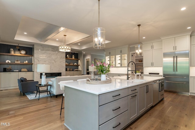 kitchen with stainless steel built in refrigerator, wood-type flooring, and a center island with sink