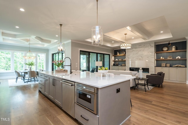 kitchen with sink, light wood-type flooring, pendant lighting, gray cabinets, and a kitchen island with sink