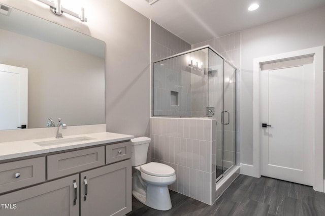 bathroom with toilet, hardwood / wood-style floors, a shower with shower door, and vanity