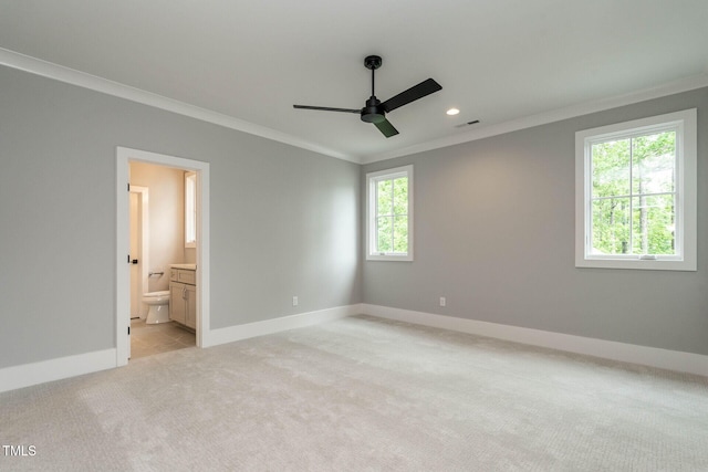 unfurnished bedroom featuring ensuite bathroom, multiple windows, light colored carpet, and ceiling fan