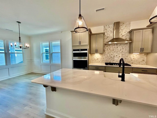 kitchen featuring wall chimney range hood, hardwood / wood-style floors, decorative light fixtures, and appliances with stainless steel finishes