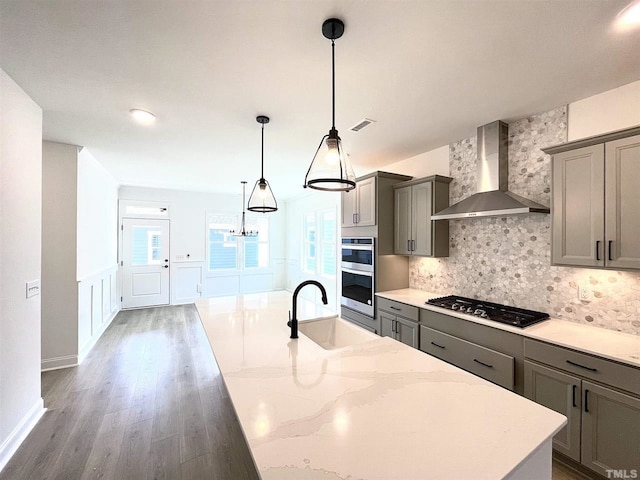 kitchen with tasteful backsplash, wall chimney exhaust hood, appliances with stainless steel finishes, sink, and pendant lighting