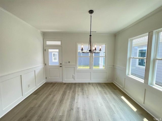 unfurnished dining area featuring crown molding, an inviting chandelier, and hardwood / wood-style floors