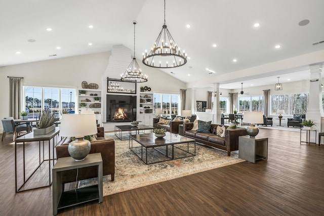 living room with a wealth of natural light, dark wood-type flooring, ornate columns, and a notable chandelier