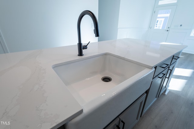 interior details with gray cabinetry, light stone counters, sink, and hardwood / wood-style floors