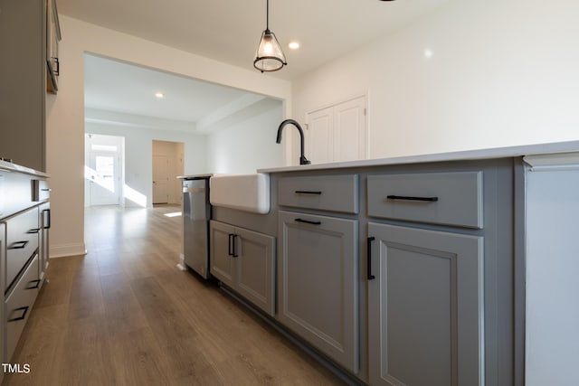 kitchen featuring hanging light fixtures, stainless steel dishwasher, an island with sink, dark hardwood / wood-style flooring, and gray cabinets