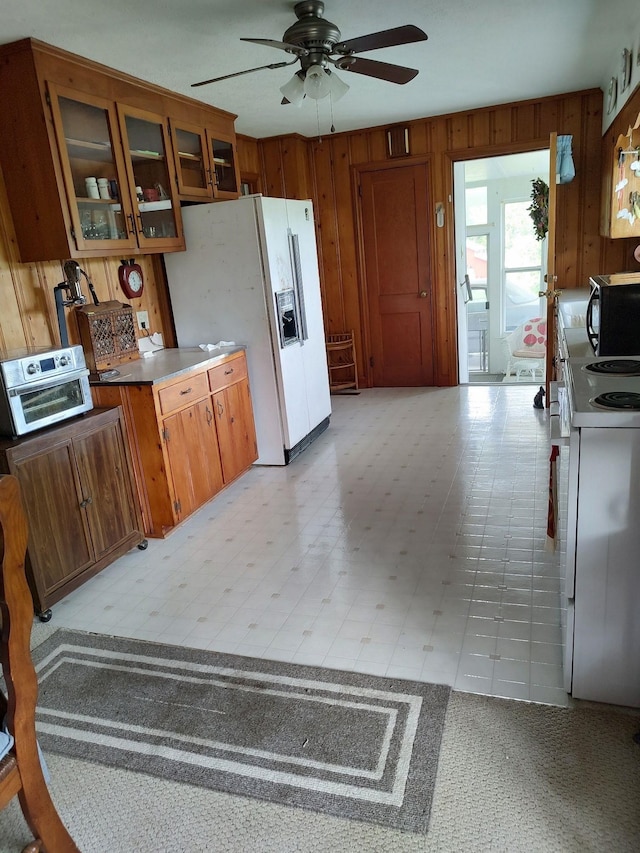 kitchen featuring white refrigerator with ice dispenser, ceiling fan, range, wooden walls, and light tile floors