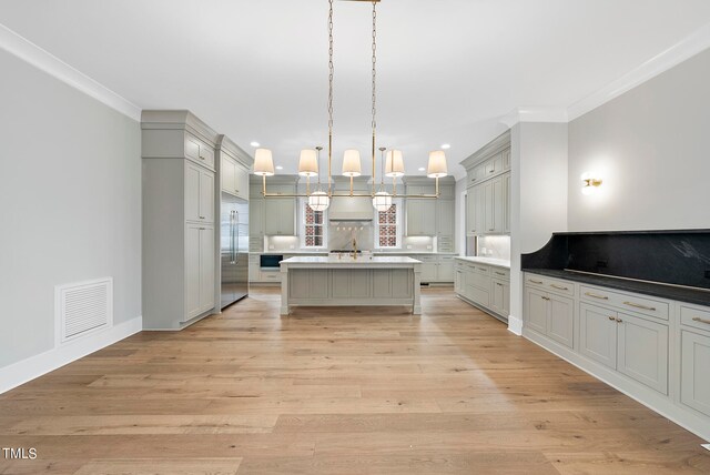 kitchen featuring decorative light fixtures, a center island with sink, light hardwood / wood-style flooring, built in refrigerator, and crown molding