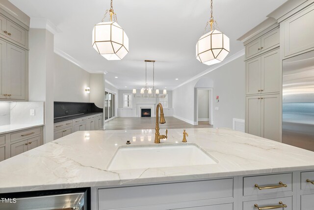 kitchen featuring decorative light fixtures, light stone countertops, sink, gray cabinets, and a center island with sink