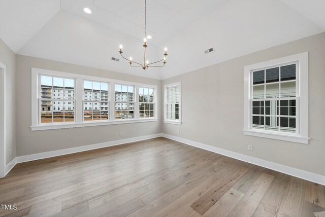 unfurnished room with light wood-type flooring, vaulted ceiling, plenty of natural light, and a chandelier