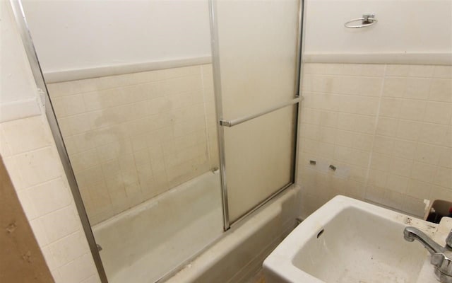 bathroom featuring sink, tile walls, and combined bath / shower with glass door