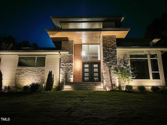 exterior entry at twilight featuring stone siding and a lawn