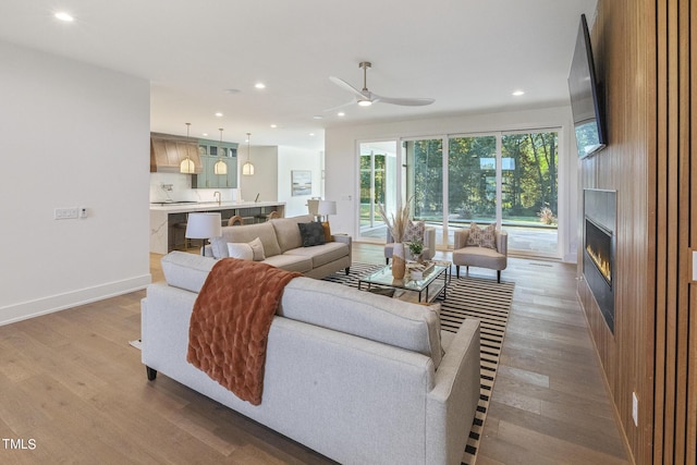 living area featuring a ceiling fan, wood finished floors, baseboards, recessed lighting, and a large fireplace