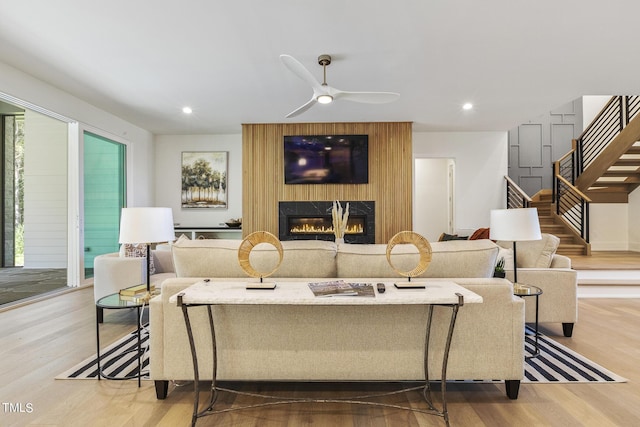 living area featuring a ceiling fan, wood finished floors, recessed lighting, stairway, and a large fireplace