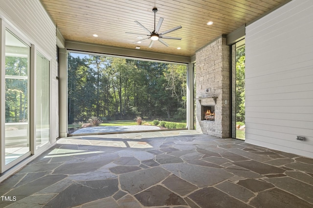 unfurnished sunroom featuring wooden ceiling, an outdoor stone fireplace, and ceiling fan