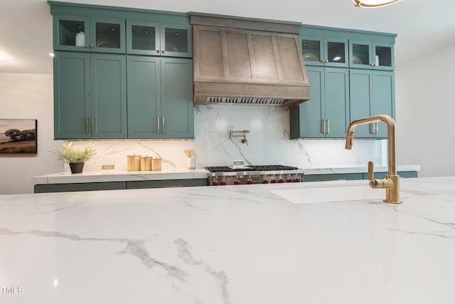 kitchen featuring tasteful backsplash, custom range hood, glass insert cabinets, and light stone countertops