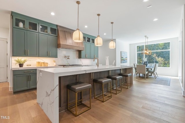 kitchen with decorative backsplash, light stone counters, light wood-style flooring, and custom exhaust hood