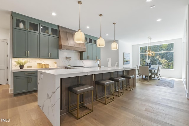 kitchen with custom range hood, light wood-style flooring, tasteful backsplash, and light stone countertops