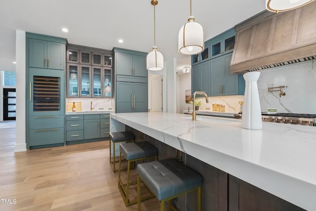 kitchen featuring light stone counters, wine cooler, custom range hood, a sink, and paneled built in refrigerator