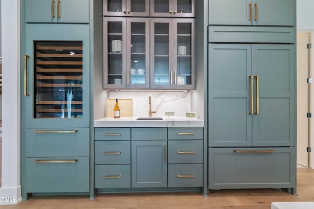 bar featuring built in fridge, a sink, light wood-type flooring, decorative backsplash, and indoor wet bar