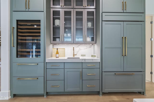 bar with light wood-type flooring, beverage cooler, a sink, tasteful backsplash, and built in fridge