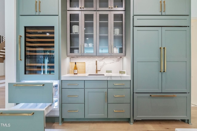 bar with wine cooler, built in refrigerator, a sink, light wood finished floors, and tasteful backsplash