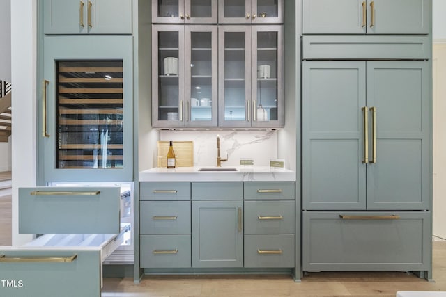 bar with a sink, decorative backsplash, wine cooler, built in fridge, and light wood-type flooring