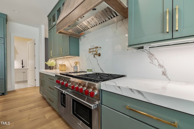 kitchen featuring range with two ovens, custom range hood, green cabinetry, and light wood finished floors