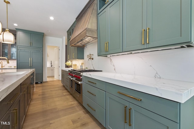 kitchen with high end appliances, premium range hood, a sink, decorative backsplash, and light wood-type flooring