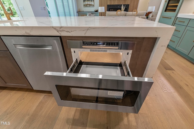 interior details with light stone counters, green cabinetry, light wood-style flooring, and stainless steel dishwasher