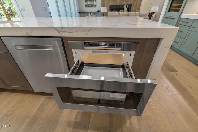 kitchen with plenty of natural light, light stone countertops, light wood-type flooring, and stainless steel dishwasher