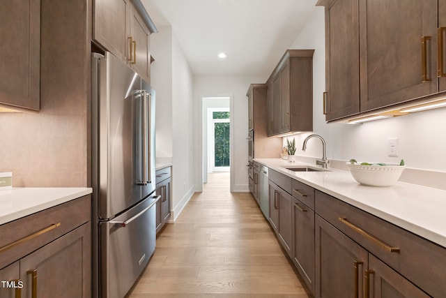 kitchen featuring light wood finished floors, baseboards, stainless steel appliances, light countertops, and a sink