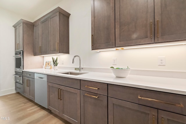 kitchen featuring appliances with stainless steel finishes, light countertops, light wood-type flooring, a sink, and a warming drawer