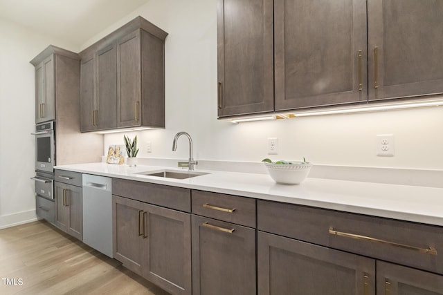 kitchen with a sink, light countertops, dark brown cabinets, appliances with stainless steel finishes, and light wood-type flooring