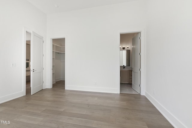 unfurnished bedroom featuring a walk in closet, baseboards, wood finished floors, a closet, and ensuite bath