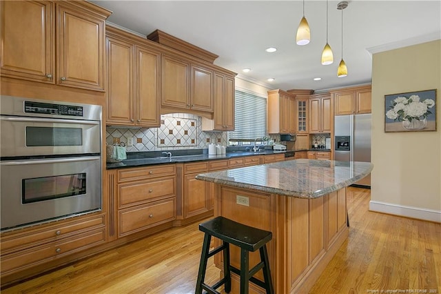 kitchen with dark stone countertops, stainless steel appliances, light hardwood / wood-style flooring, a center island, and hanging light fixtures