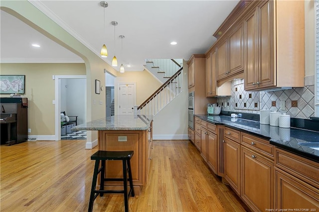 kitchen with backsplash, pendant lighting, light hardwood / wood-style floors, and dark stone countertops