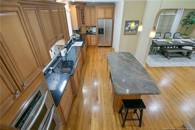 kitchen featuring stainless steel fridge, dark stone counters, hanging light fixtures, and light hardwood / wood-style floors