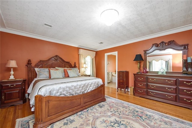 bedroom with light hardwood / wood-style floors, ensuite bathroom, and ornamental molding