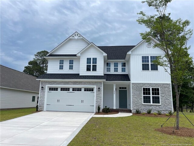 view of front facade featuring driveway, a front yard, stone siding, and a garage