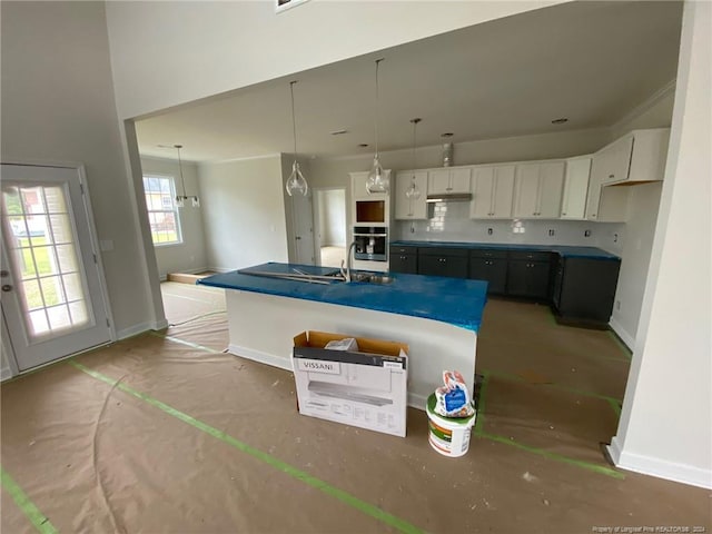 kitchen featuring stainless steel oven, sink, pendant lighting, a center island with sink, and white cabinets