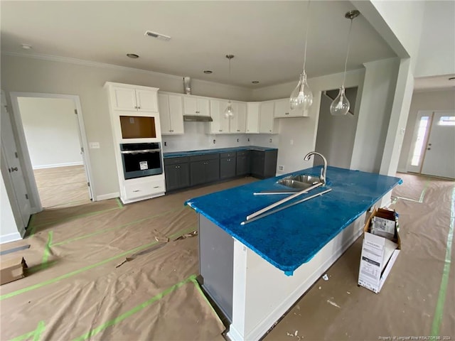 kitchen featuring a center island with sink, oven, sink, hanging light fixtures, and white cabinetry