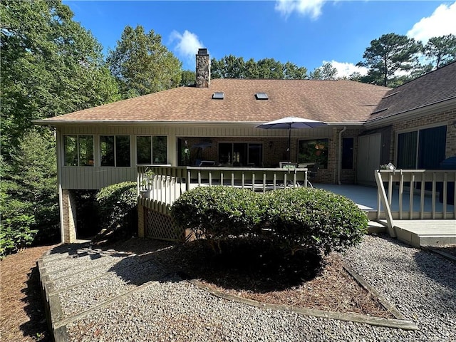 rear view of property with a chimney, a wooden deck, brick siding, and roof with shingles
